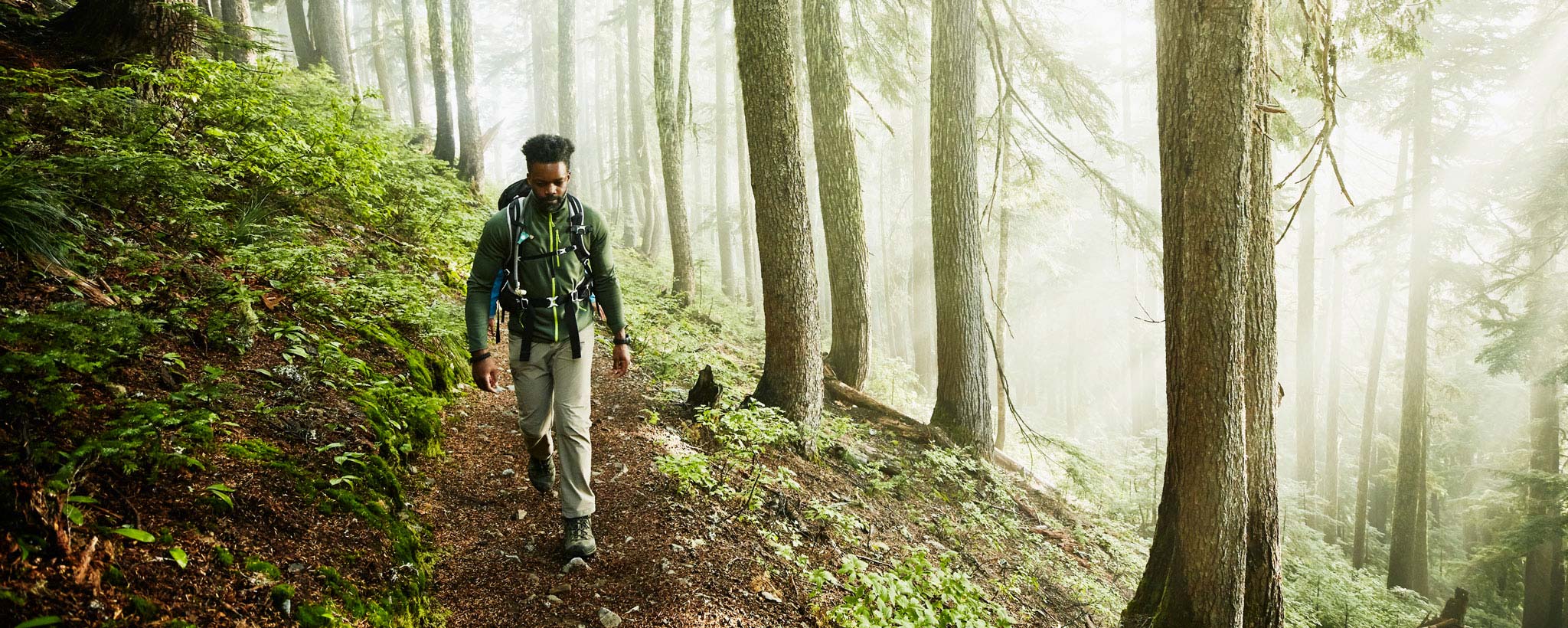 Man hiking along trail in forest on foggy morning