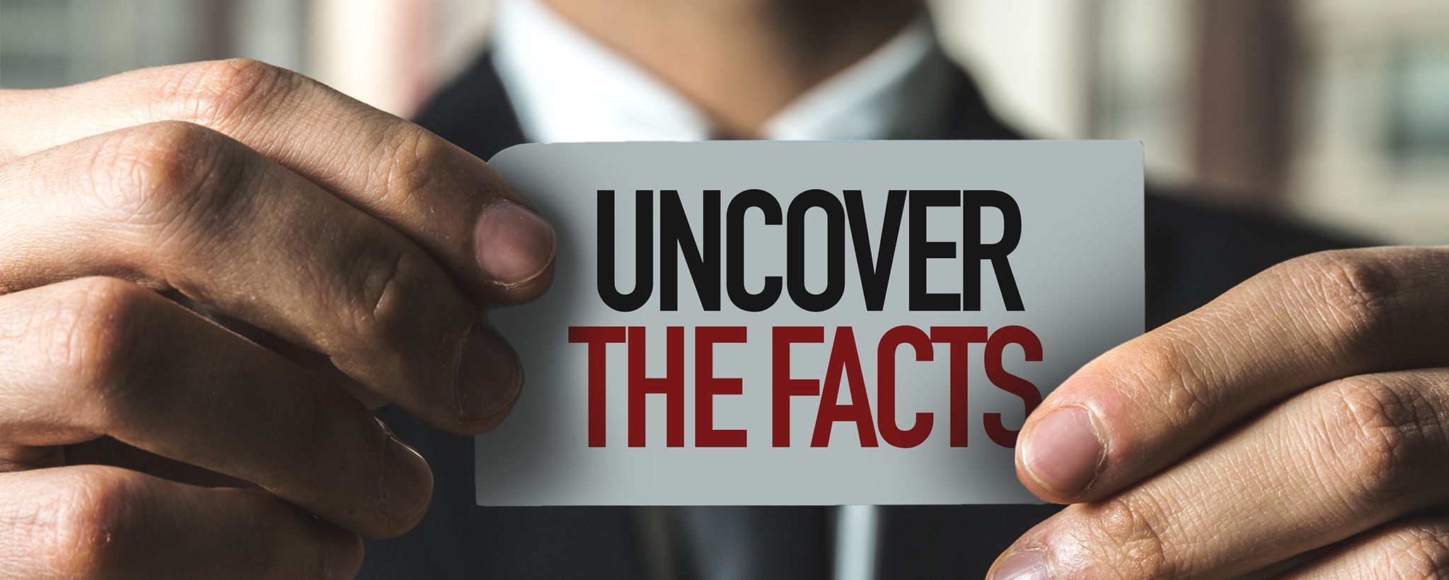 A photograph of a hand holding a rectangular tag that reads uncover the facts.