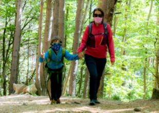 Mom and son holding hands wearing face masks due to COVID-19 walking on a trail