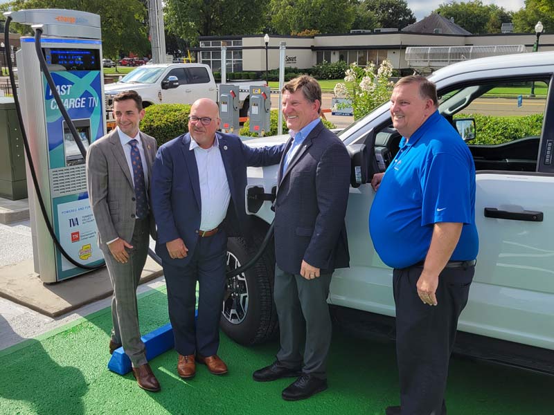 Mayor Jake Bynum, David Salyers, Jeff Lyash, Mayor Randy Brundige in front of an EV