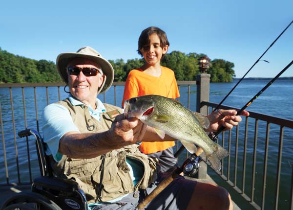 The dad is holding up a fish he just caught while fishing